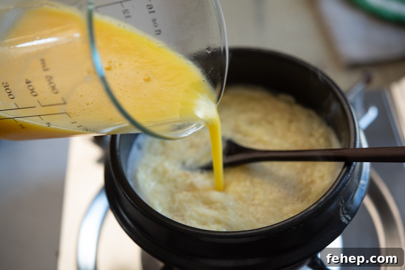 Pouring egg mixture into boiling chicken stock in a ttukbaegi to make Korean steamed egg.