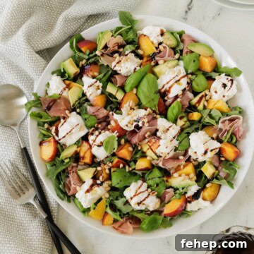 Colorful summer salad or burrata cheese, golden peaches, greens, basil, and balsamic dressing.