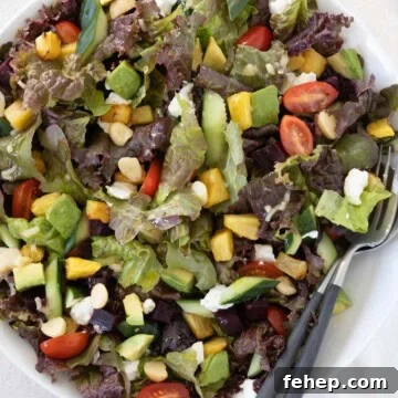 Color Hawaiian salad with tomatoes, avocado, pineapple, beets. macadamia nuts and more in a bowl with utensils.