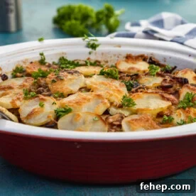 A red baking dish of boulangere potatoes, or potato bake with bacon, on a blue background and with a blue and white striped tea towel in the background