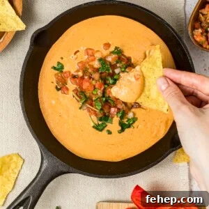 Viral high-protein cottage cheese queso dip with a woman's hands dipping into the dip with a tortilla chip.