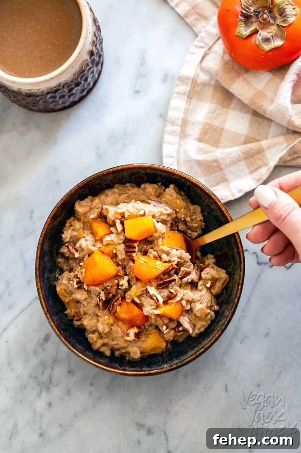 Ceramic bowl filled with persimmon oatmeal, and golden spoon, with a cup of coffee
