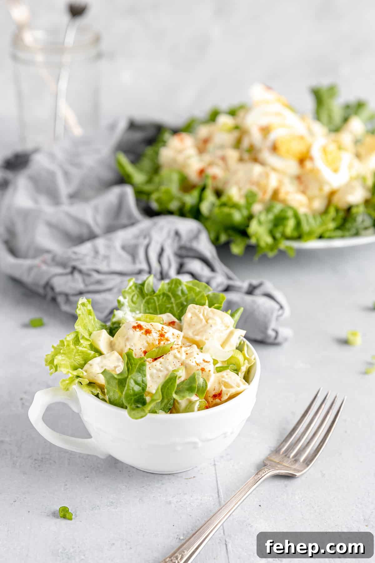A Serving of Potato Salad in a Mug with the Remaining Salad on a Plate in the Background