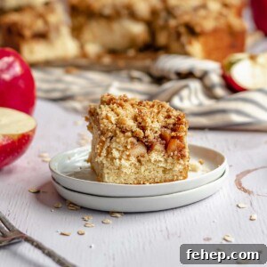 Slice of apple streusel coffee cake on a plate with the rest of the cake in the background.