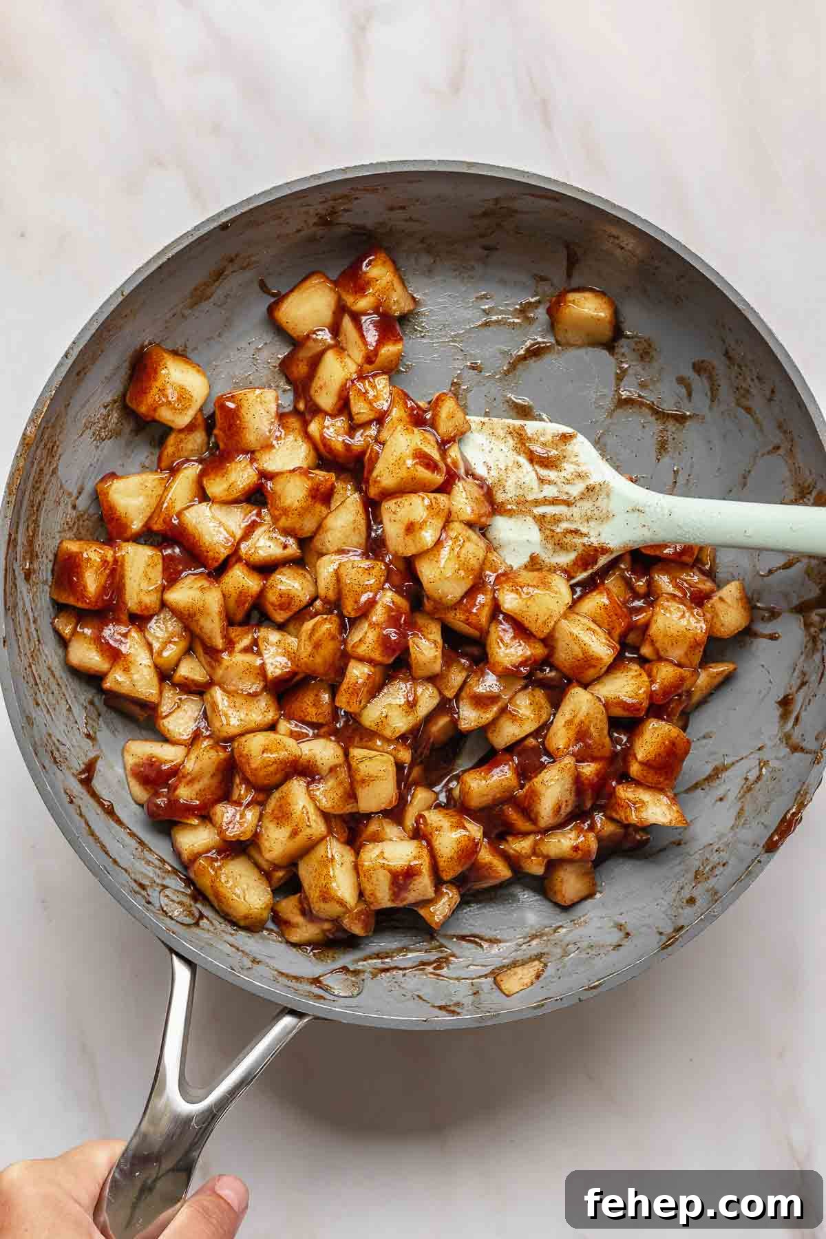 A spatula tosses spiced apples in a frying pan.