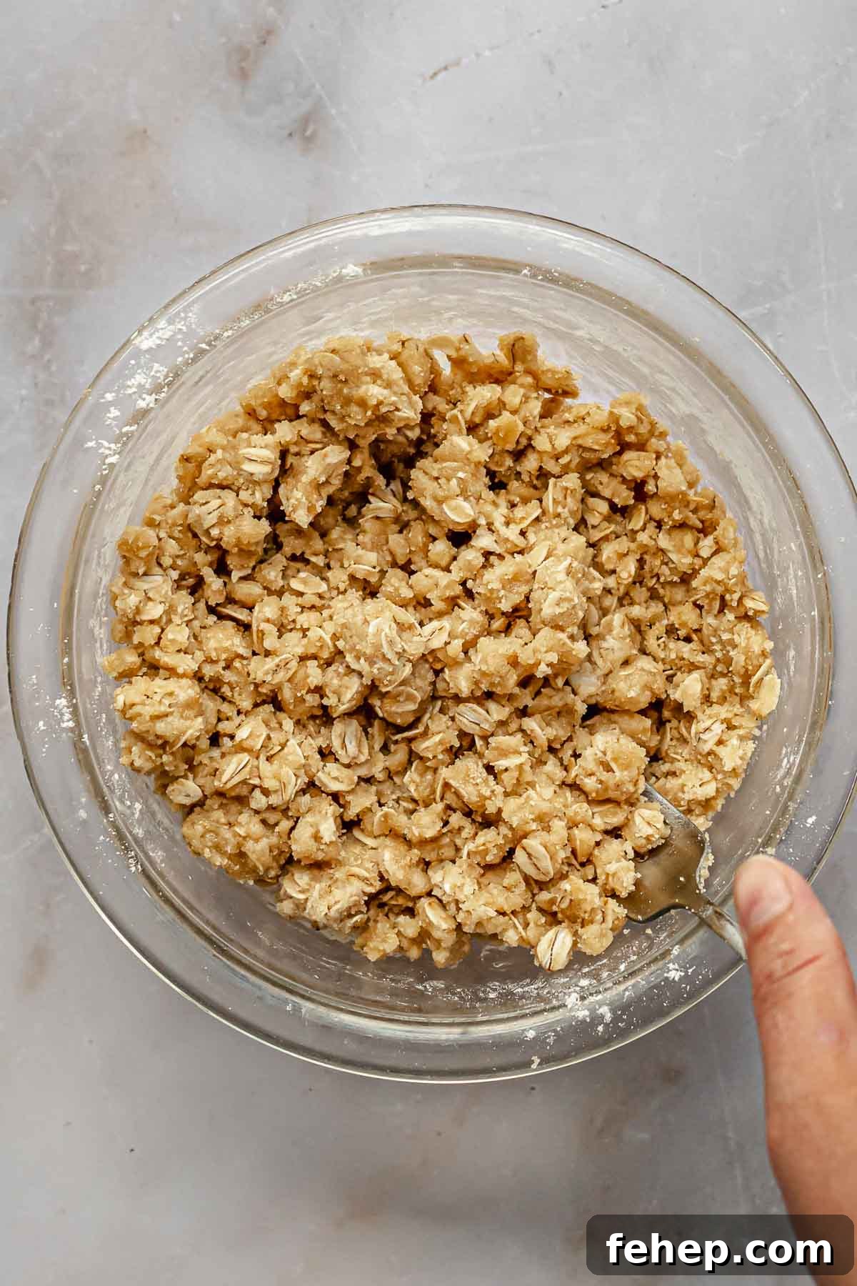 A hand mixes streusel topping in a bowl with a fork.