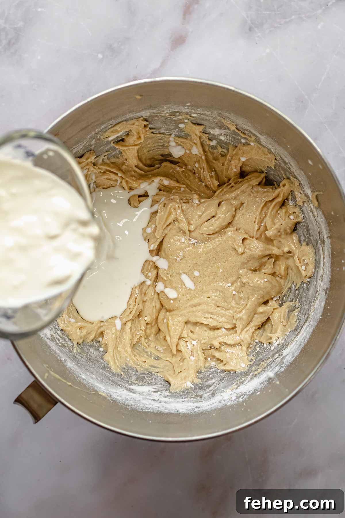 A wet measuring cup pours milk and sour cream into cake batter.
