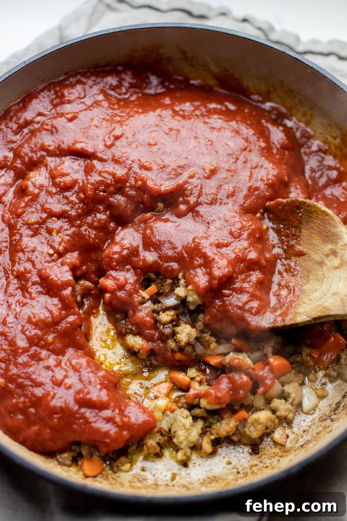 Tomato sauce being stirred with a wooden spoon.