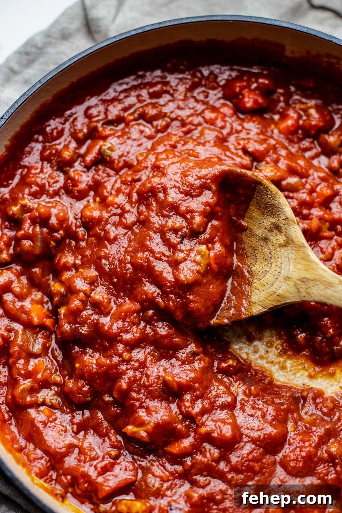 wooden spoon stirring red sauce.