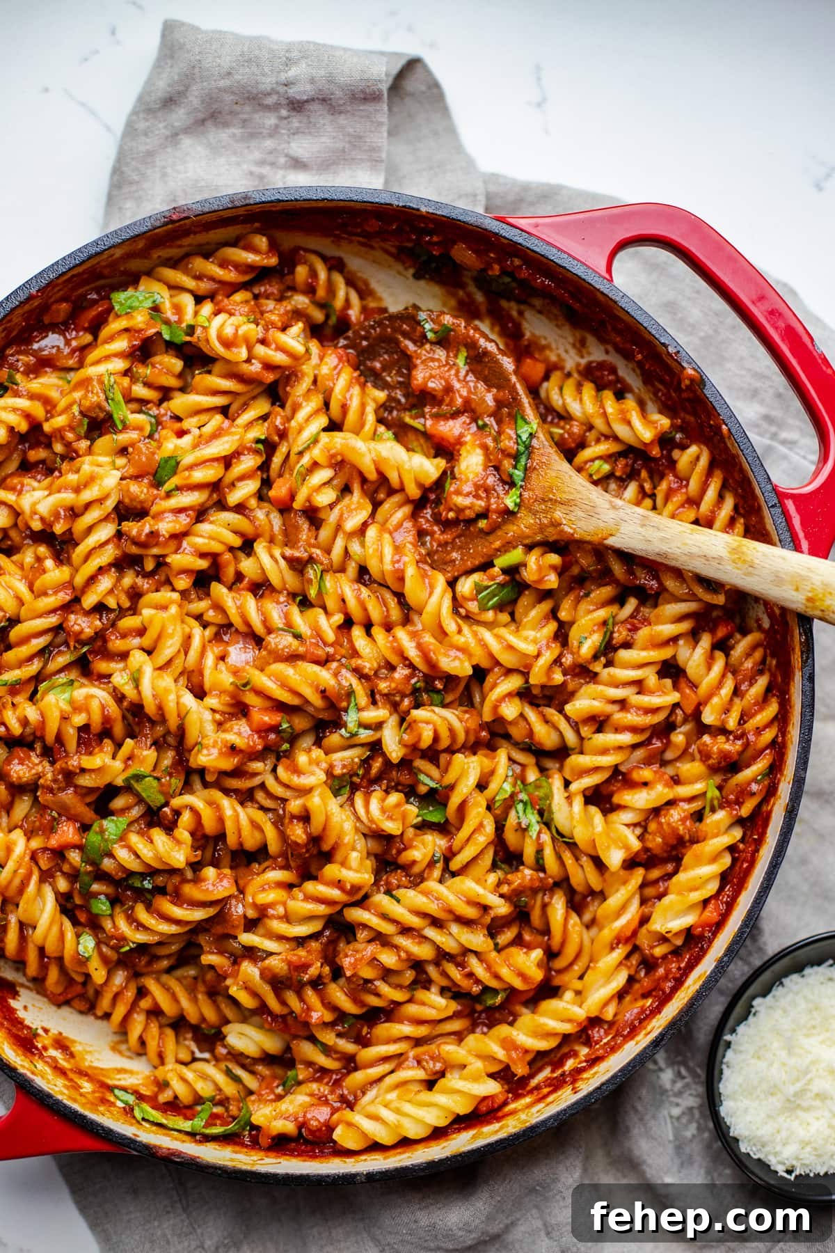 red pan with fusilli noodles in it with a wooden spoon.