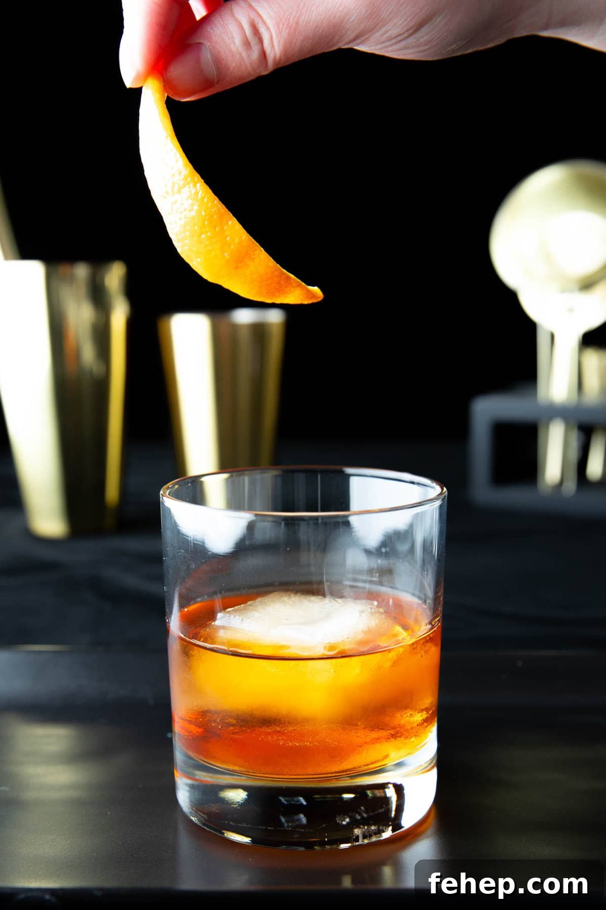 Classic Old Fashioned Cocktail Recipe: How to Make It Perfectly 3 A hand adding an orange peel garnish to this Old Fashioned drink recipe