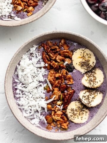 A bowl with a purple smoothie toped with coconut, granola, and banana slices.