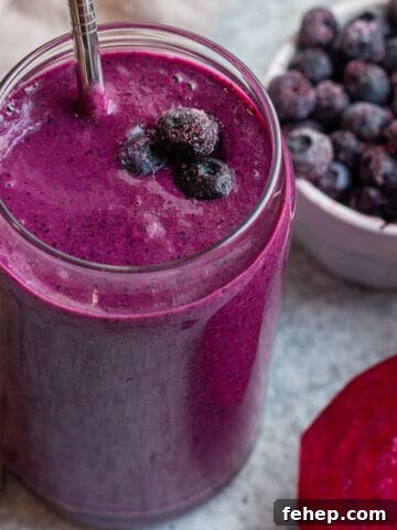 Glass cup with a purple smoothie, metal straw and frozen blueberries.
