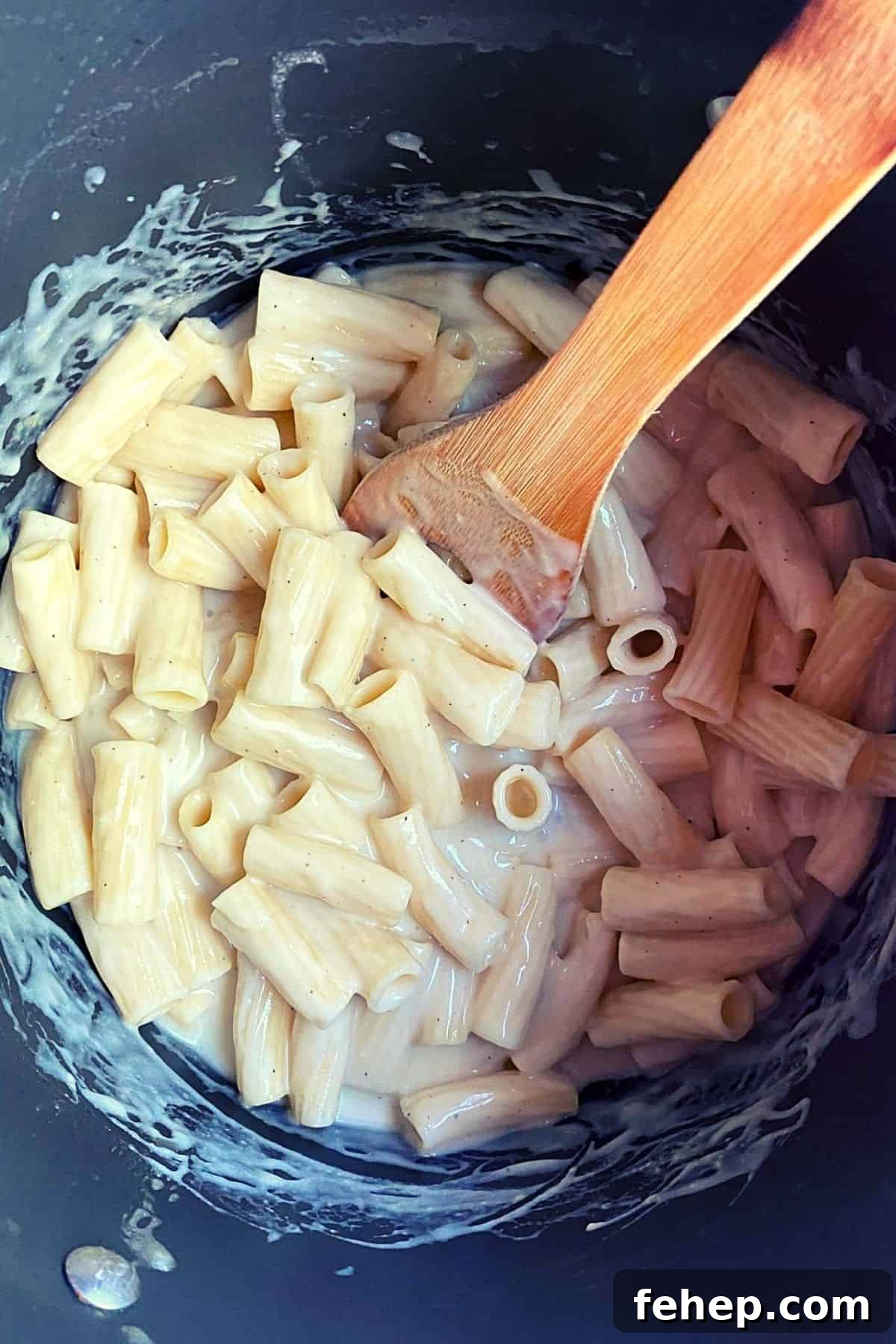 Overhead view of pasta after being mixed with cheese mixture with wood spoon