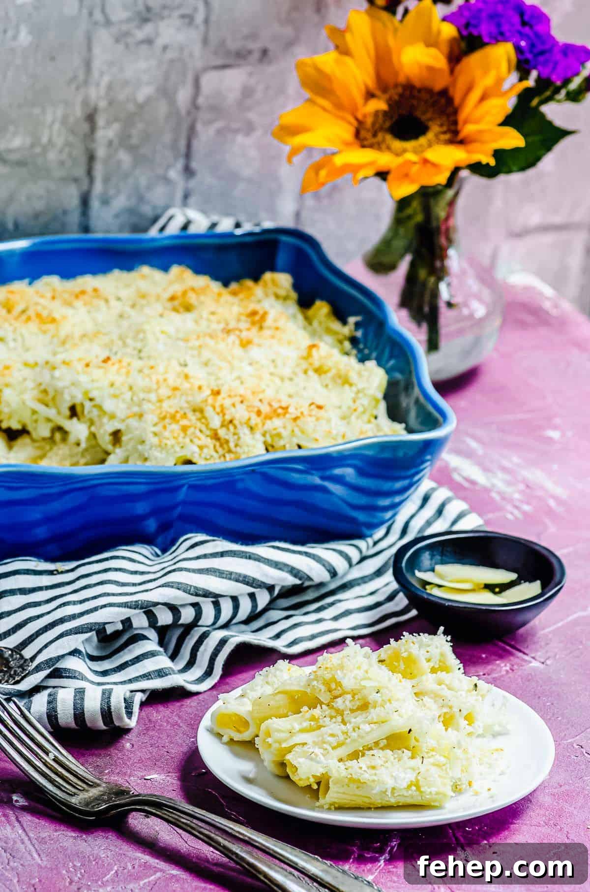 A plate of vegan mac and cheese sitting in front of a blue dish of vegan mac and cheese with a piece taken out