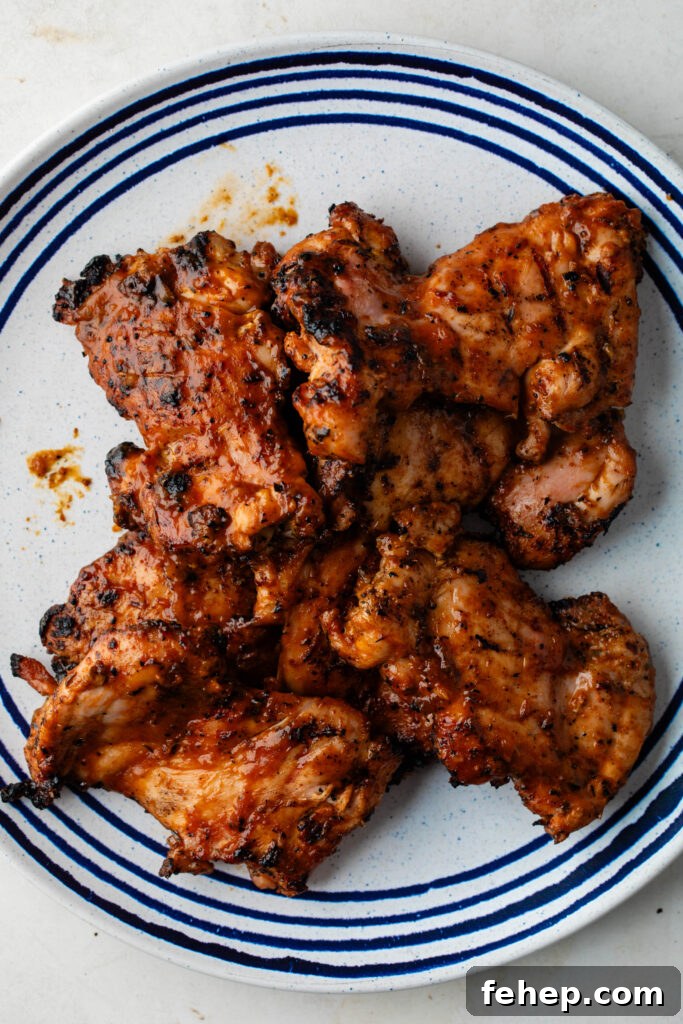 peach bbq sauce basted grill chicken thighs on a white and blue plate