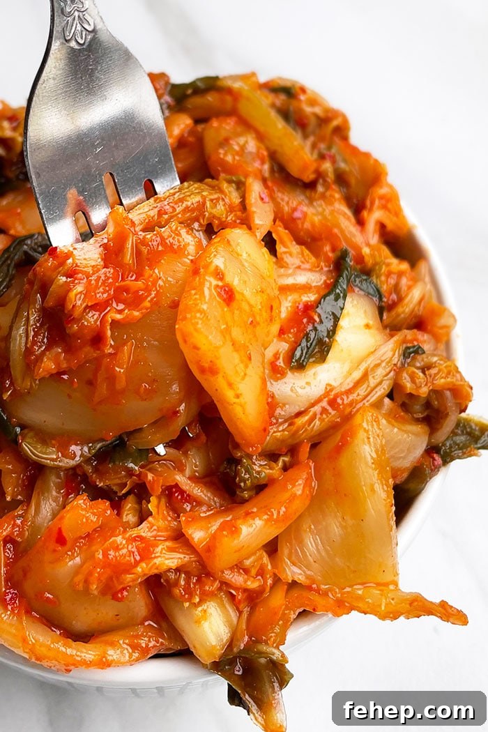 Closeup Shot of Fork Packed With Red Fermented Pickled Korean Cabbage in White Bowl on White Background