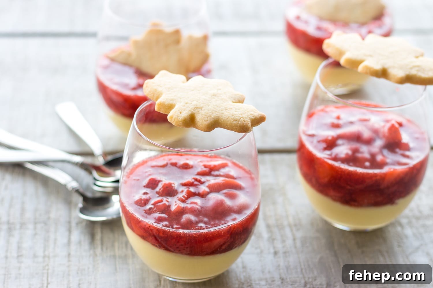 Four glasses of maple custard with strawberry compote that are topped with maple leaf shaped sugar cookies