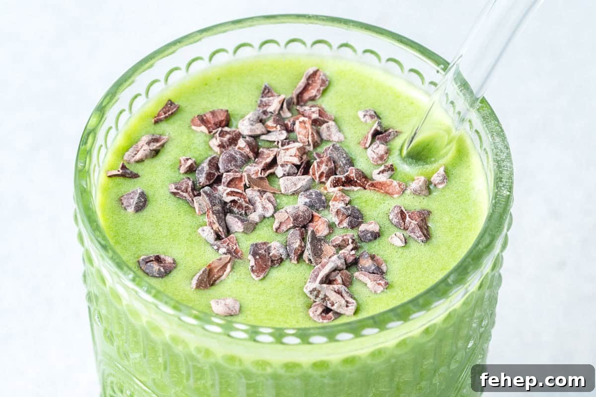shamrock smoothie in a cup topped with cocoa nibs and a glass straw in the cup.