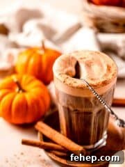 Iced coffee topped with pumpkin cold foam and spoon with mini pumpkins surrounding
