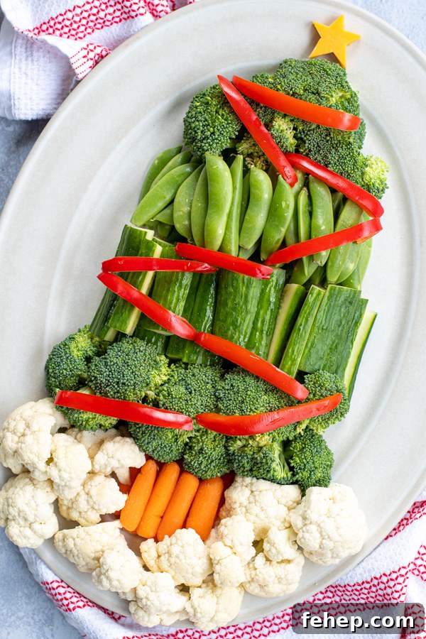 Festive Christmas Tree Vegetable Platter Ideas for Holiday Parties 5 Angled view of a platter with veggies shaped into a Christmas tree complete with red vegetables as decorations and a slice of cheese shaped like a star on top.