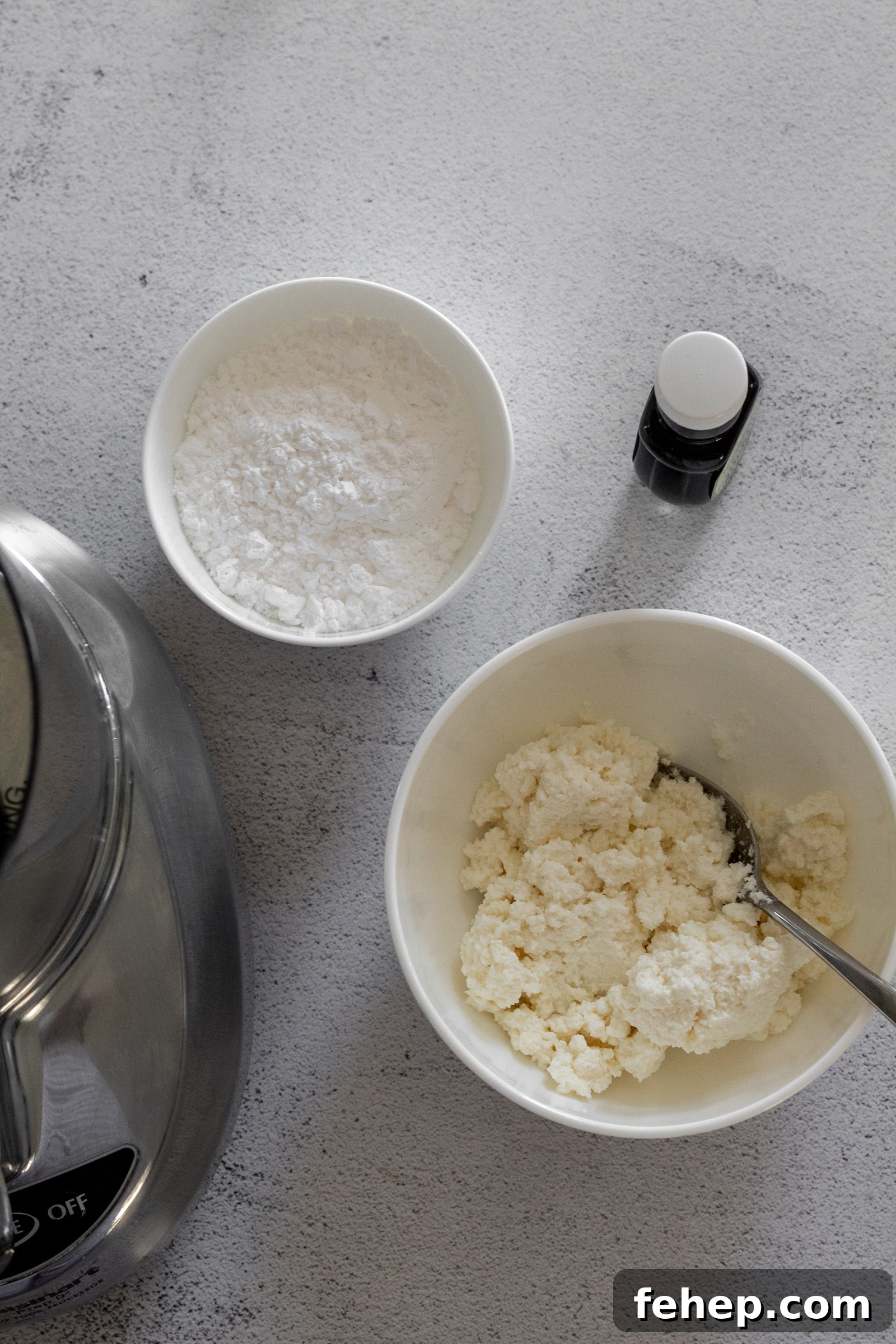 Ricotta cheese, powdered sugar and extract next to a food processor.