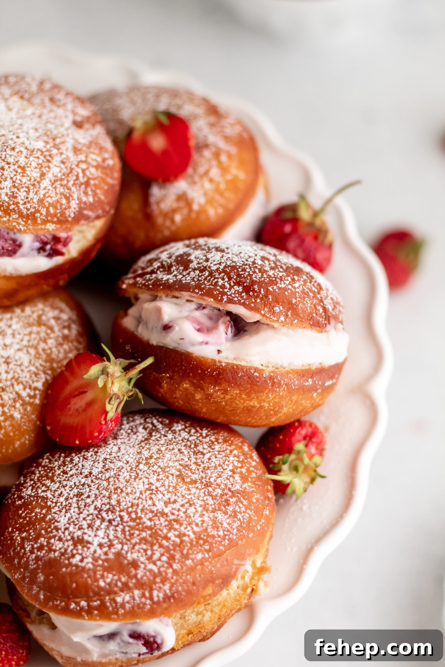 Golden brown donuts with cream and strawberries in the middle on a white platter.