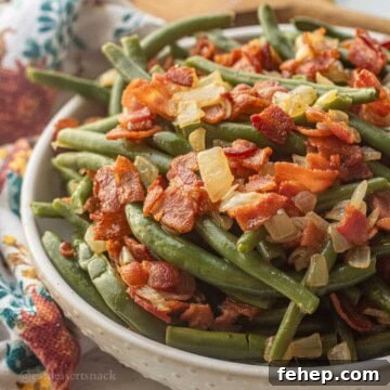 Bowl of cooked green beans with crispy bacon and cooked onions.