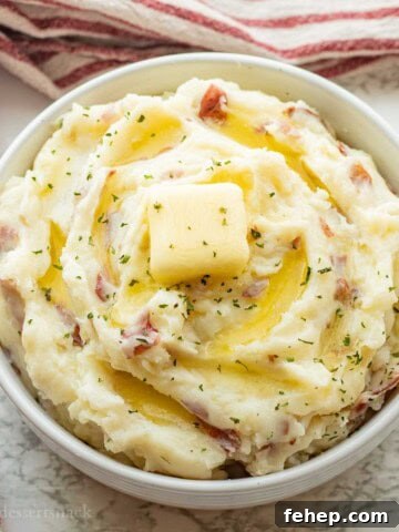 Red skin mashed potatoes with butter on top in white bowl.