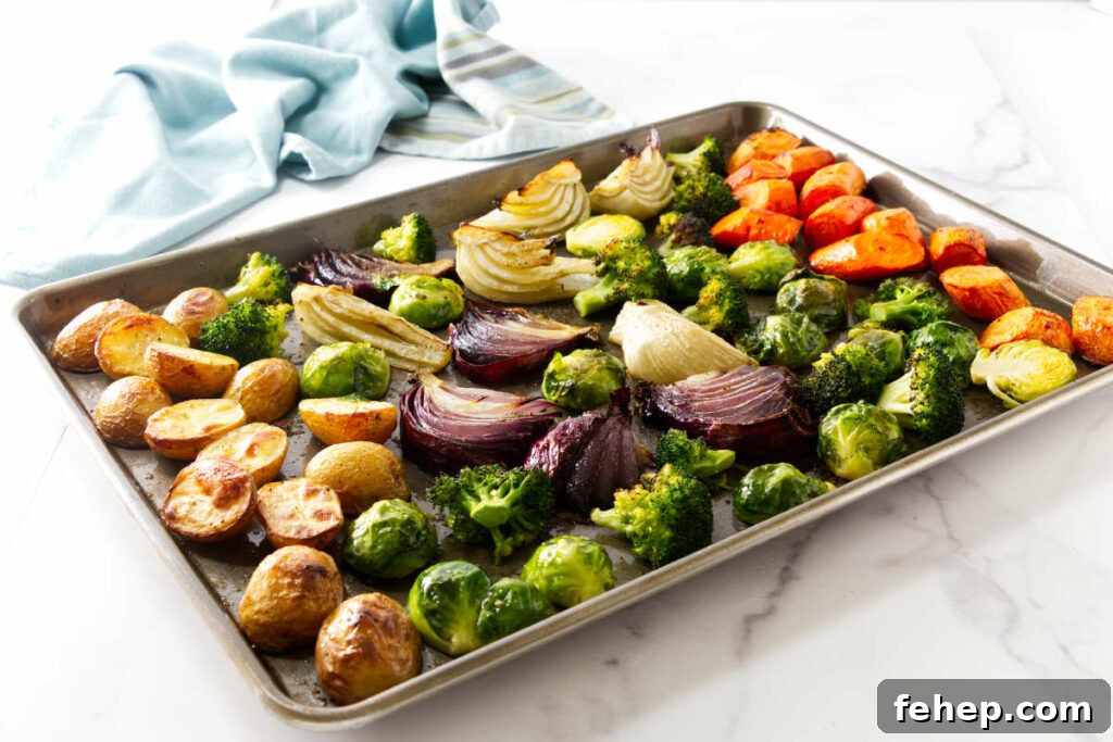 Roasted vegetables on a baking sheet, white surface, blue cloth nearby.