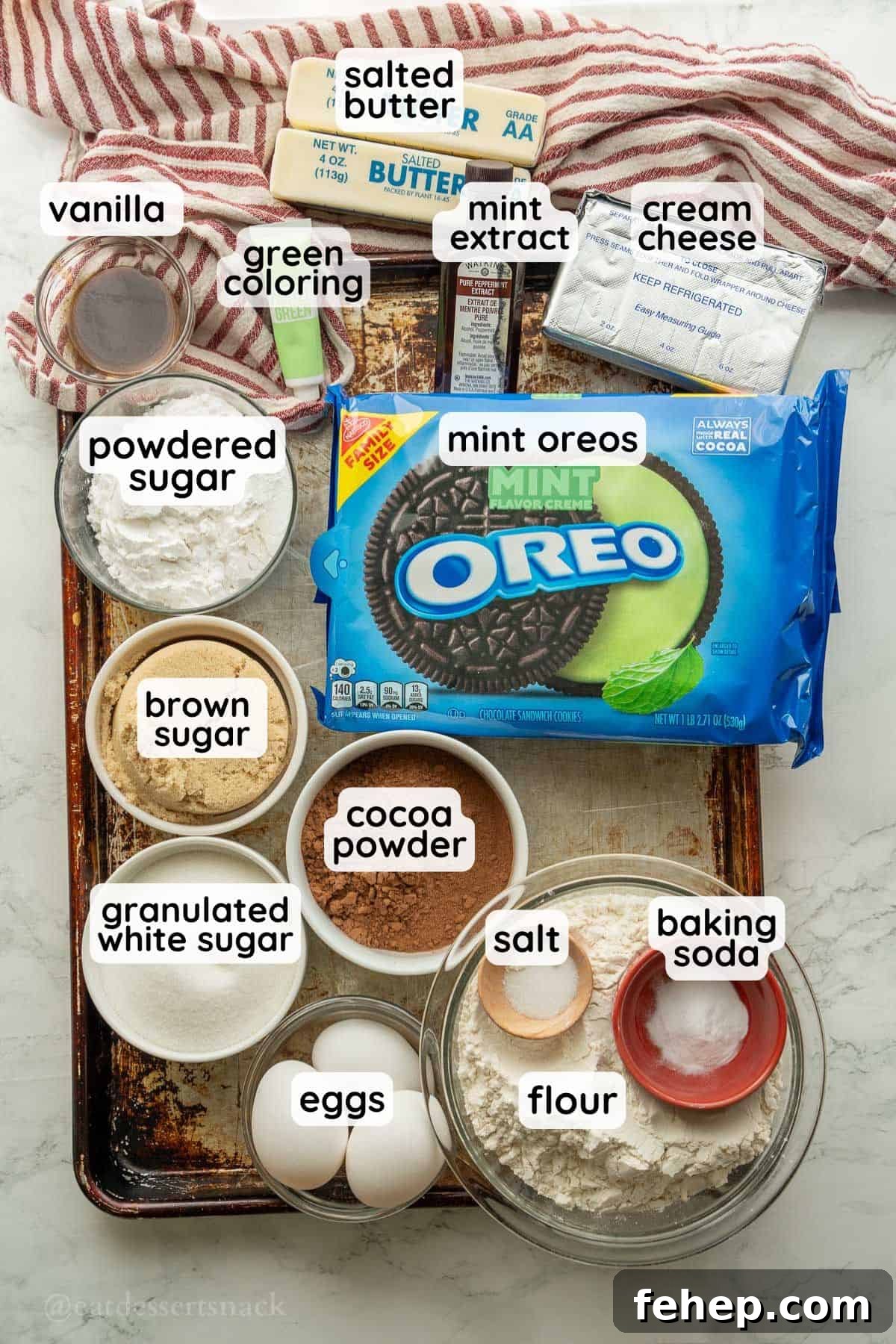 Labeled ingredients for mint cheesecake brownies in glass bowls on metal pan.