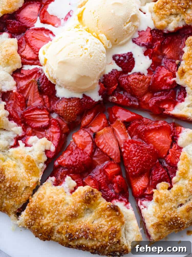 A closeup view of two slices cut out of the whole strawberry galette. Two scoops of ice cream are on top of the galette and starting to melt.
