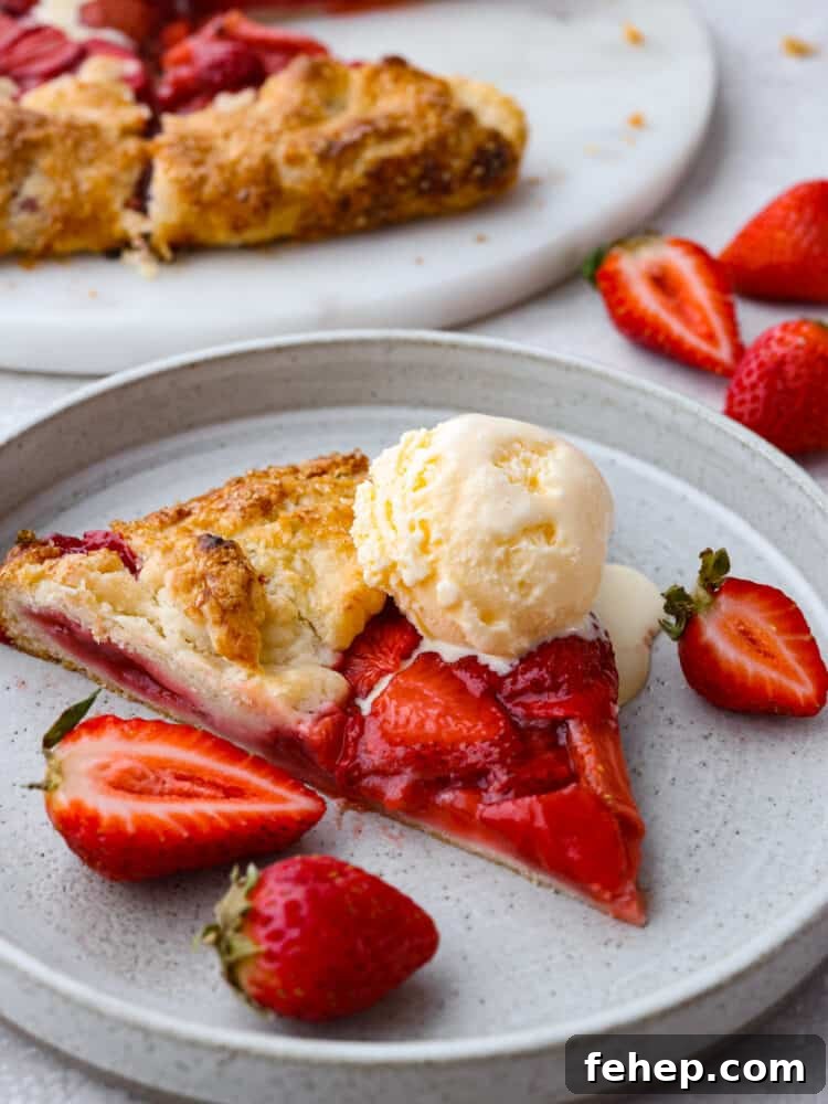 A slice of strawberry galette on a gray plate topped with a scoop of ice cream, and garnished with fresh strawberries on the side.