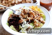 A white bowl of chipotle chicken with lettuce, corn, Pico de Gallo, black beans and shredded cheese.