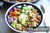 A patterned bowl filled with cilantro lime rice, rotisserie chicken, cucumbers, avocado, red onion, and tomatoes.