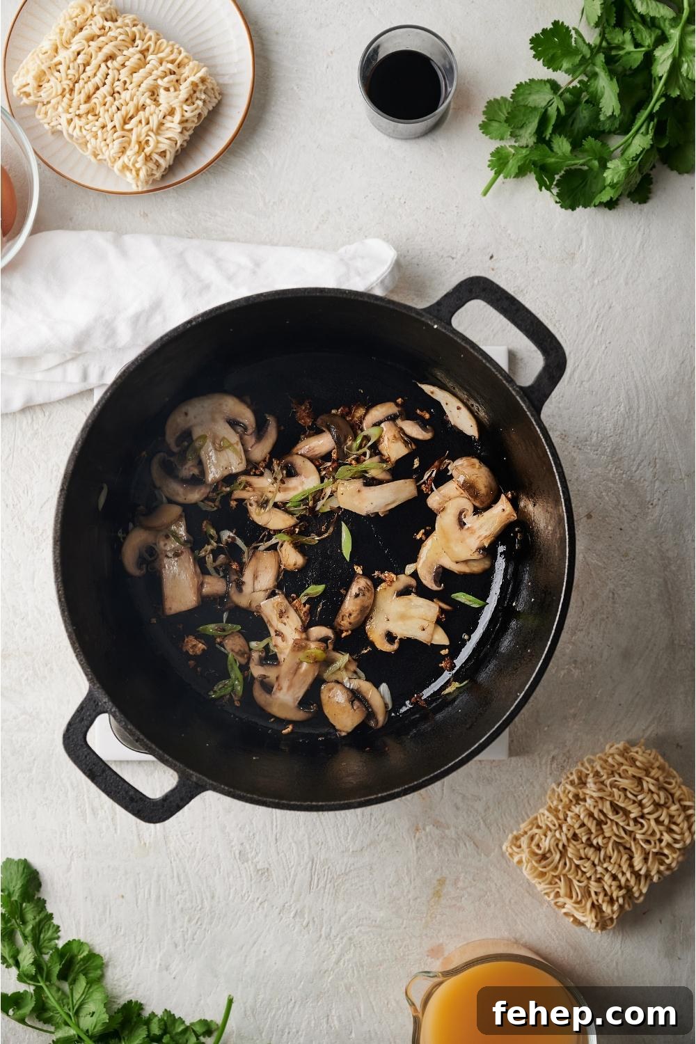 Dutch oven with sautéed mushrooms and scallions cooking in the pan, surrounded by ingredients to make beef ramen