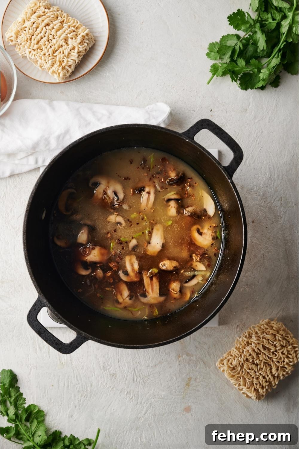 Dutch oven with beef ramen broth simmering, surrounded by raw ingredients for making beef ramen