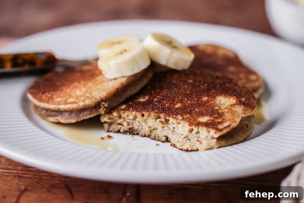 A plate of thick, soft and fluffy banana pancakes. Topped with bananas and drizzled with maple syrup.