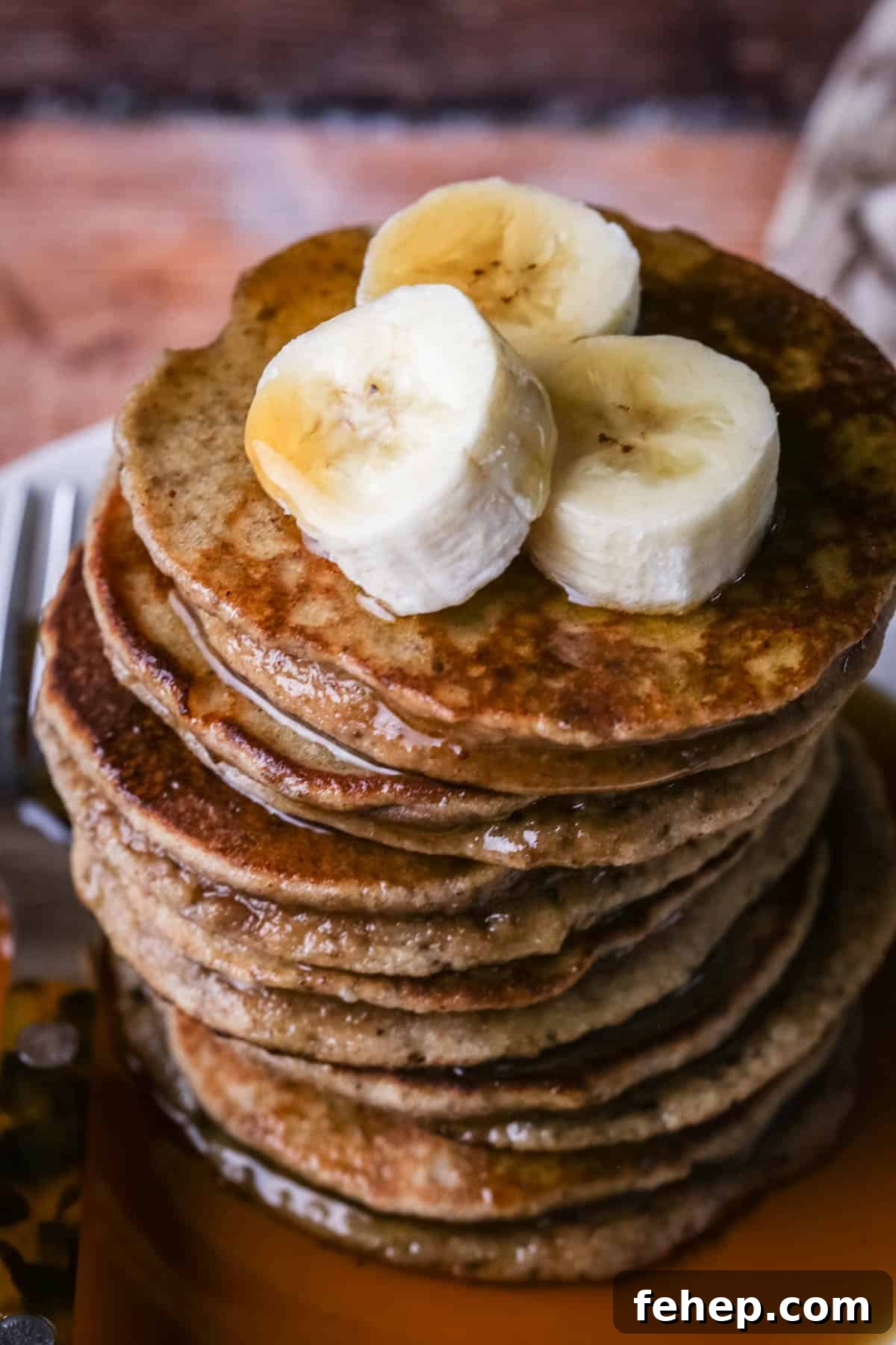A stack of thick, soft and fluffy banana pancakes. Topped with bananas and drizzled with maple syrup.