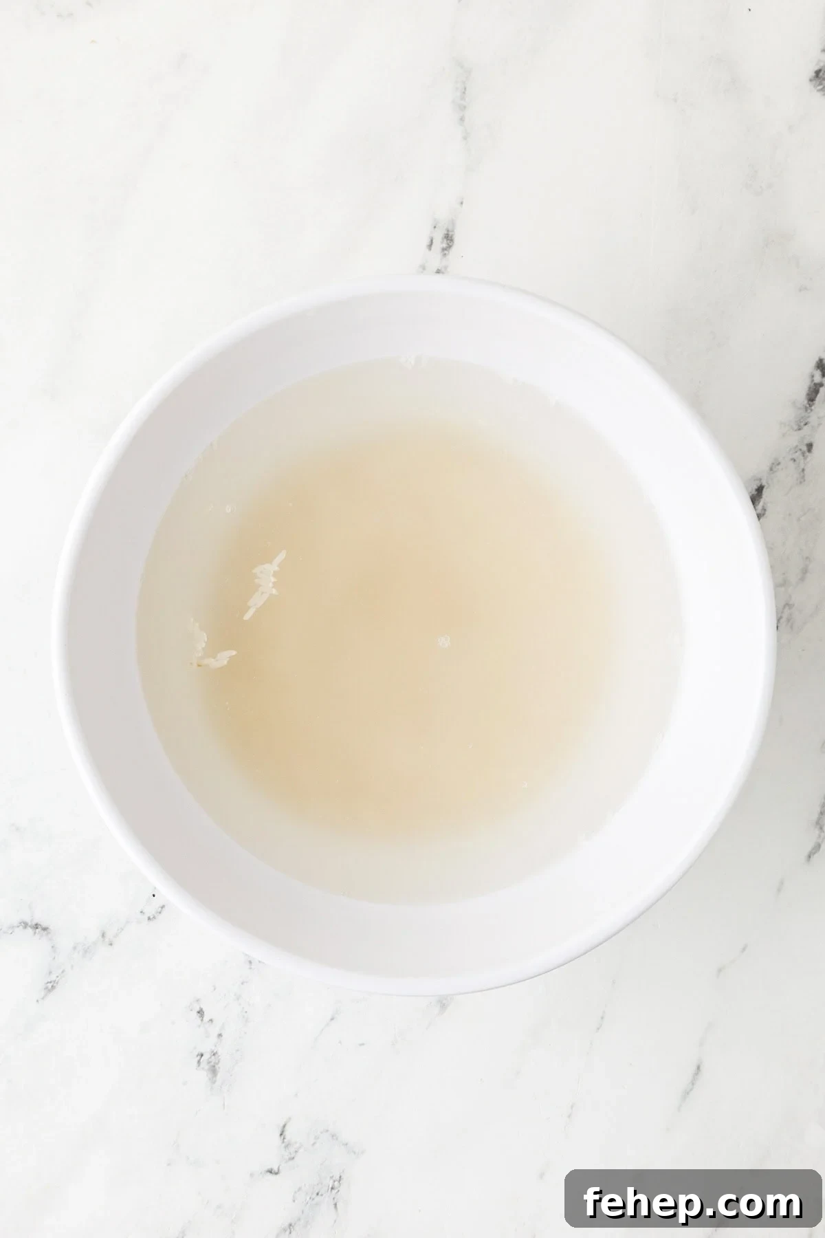 An overhead image of jasmine rice soaked in a bowl with water.