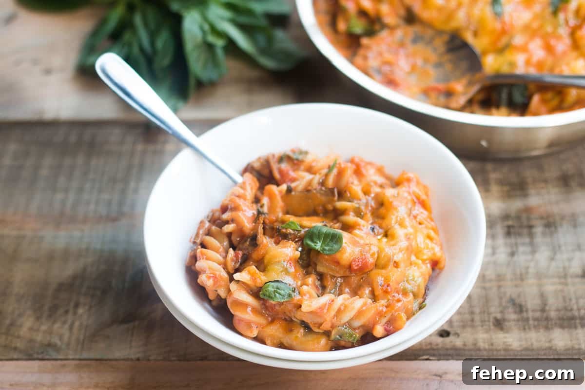 A comforting bowl of cheesy Sunday Veggie Pasta garnished with fresh basil and served in a white bowl.